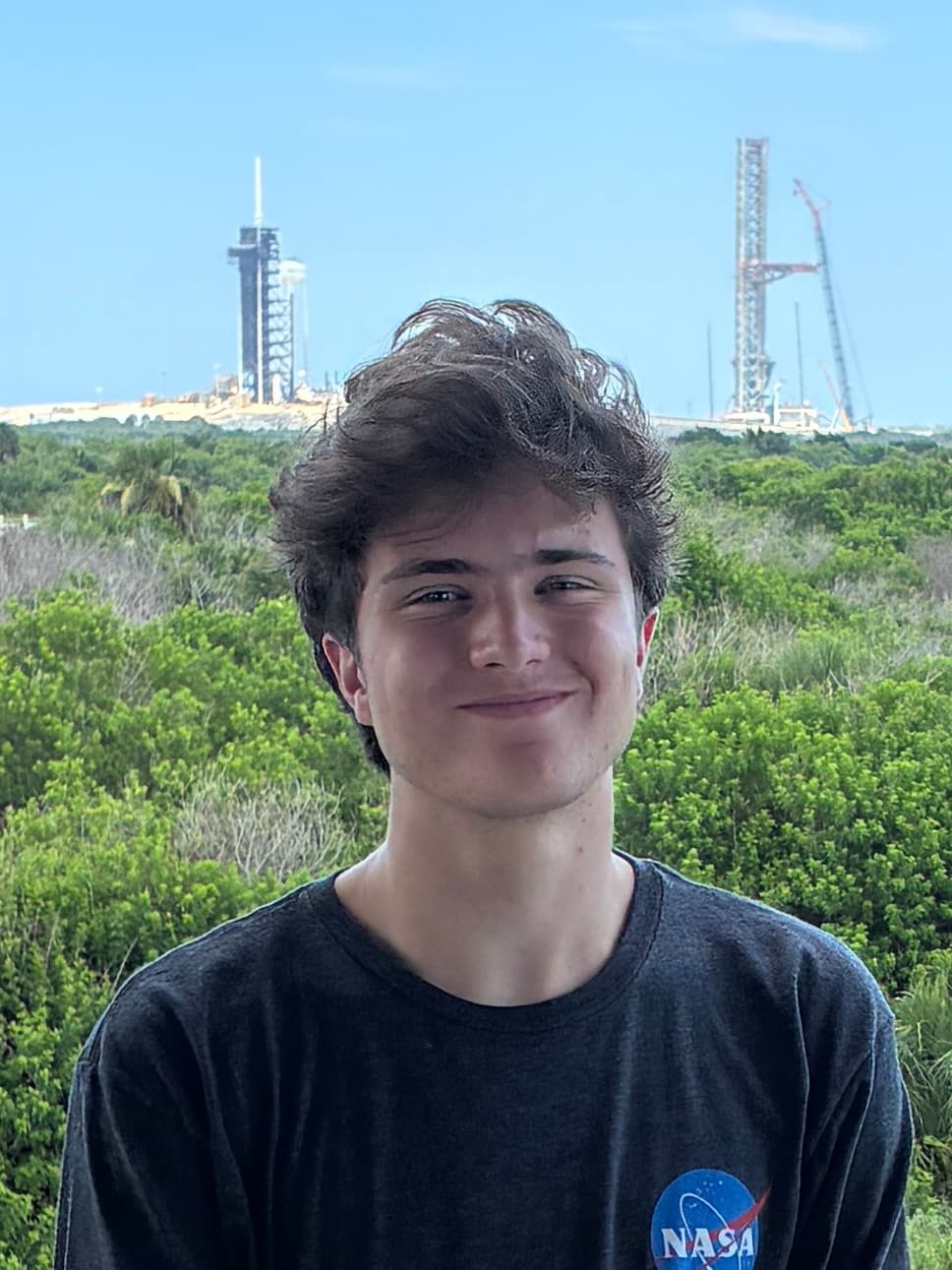 Eliot Gevers wearing a NASA shirt with launch infrastructure behind him